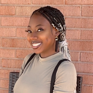 Phylicia Patton with braided hair smiling in front of a brick wall